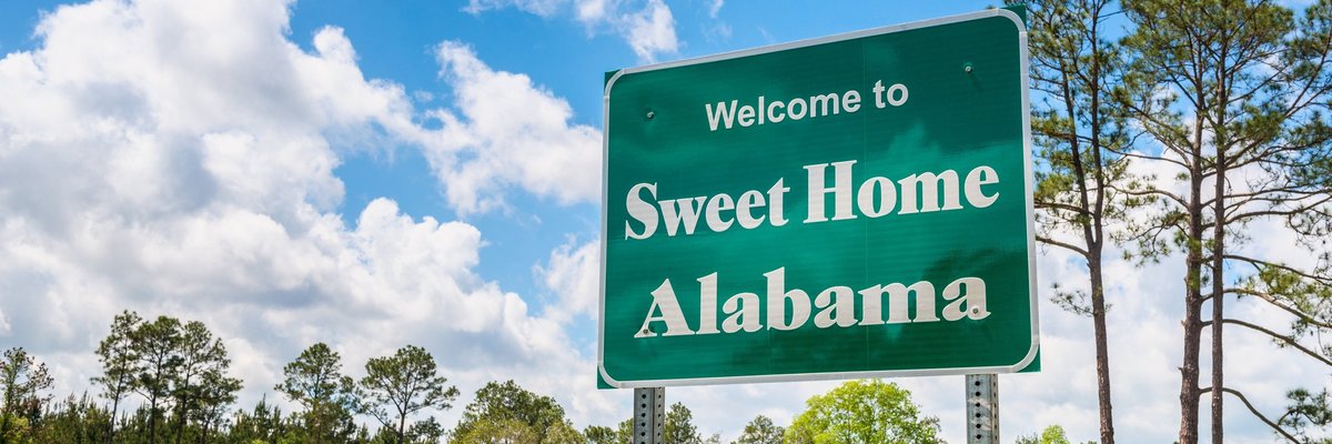 Green grass and a blue sky behind a road sign that says Welcome to Sweet Home Alabama.