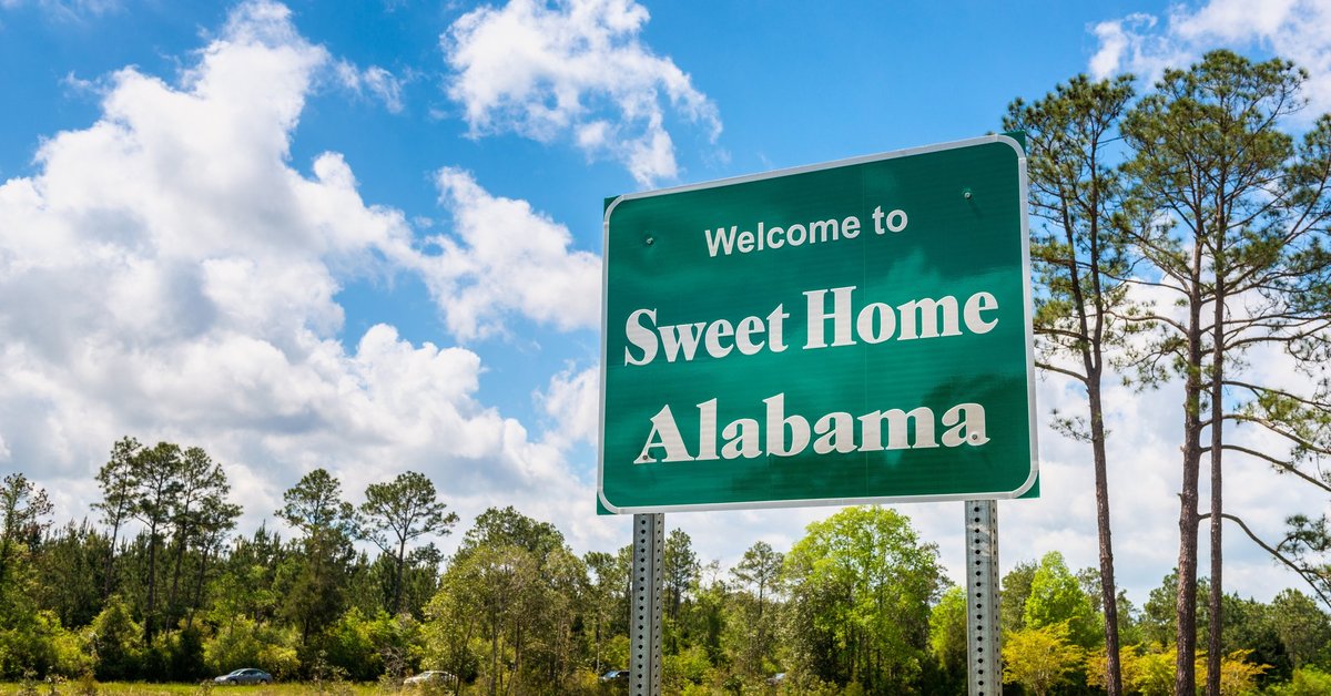 Green grass and a blue sky behind a road sign that says Welcome to Sweet Home Alabama.