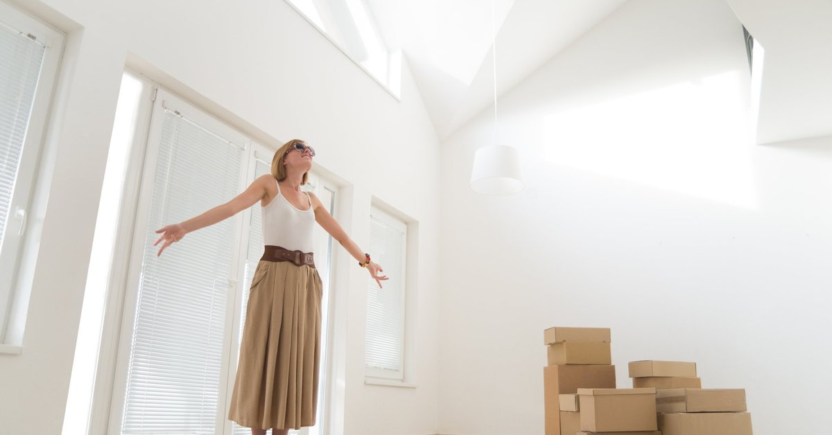 A woman celebrating with her arms out while standing next to moving boxes in her new home.