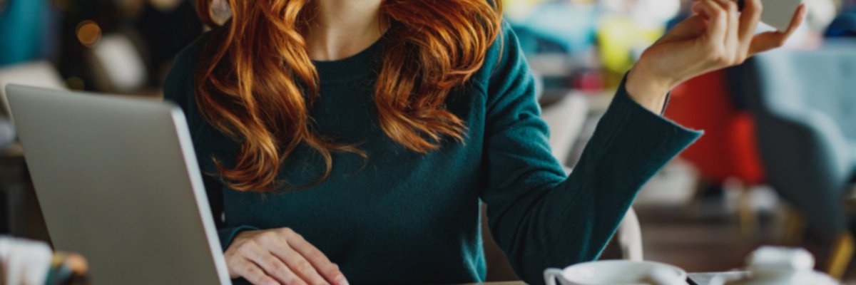 A woman sitting at a cafe table with tea and a laptop and holding out her credit card.