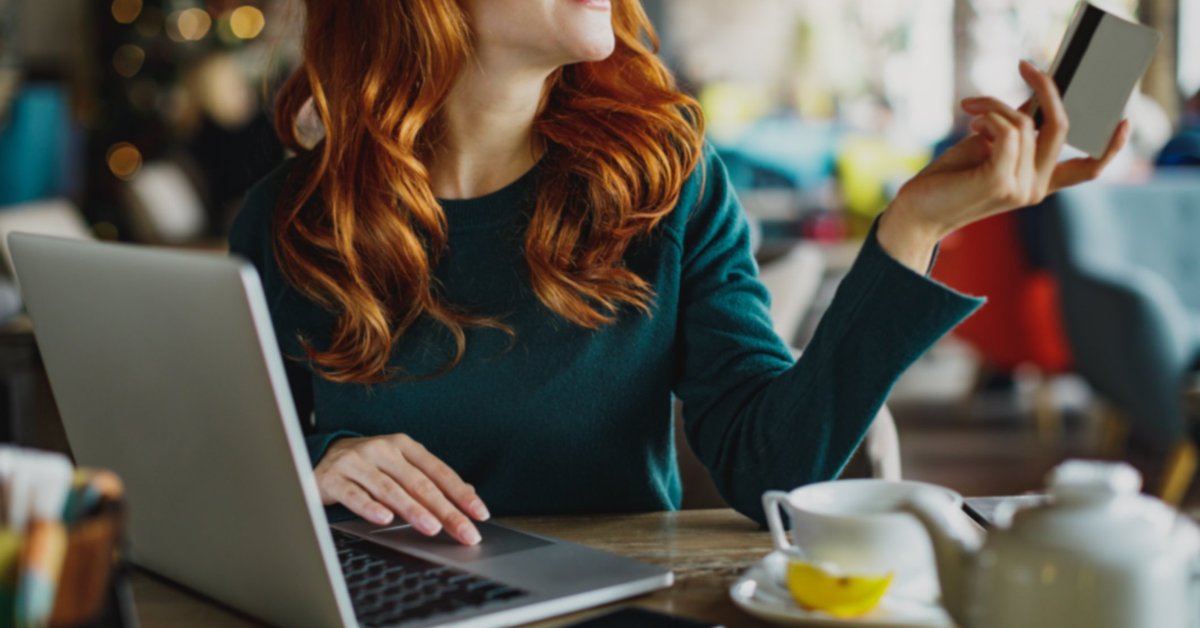 A woman sitting at a cafe table with tea and a laptop and holding out her credit card.