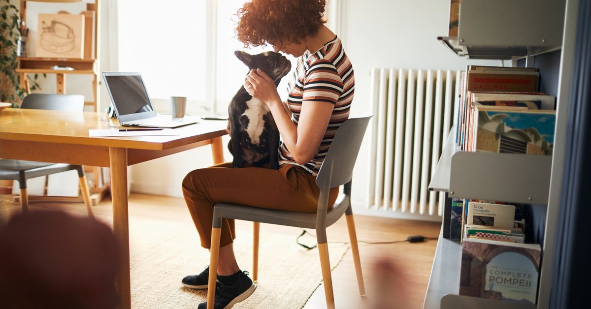 A woman sitting in her home office snuggling with a dog on her lap.