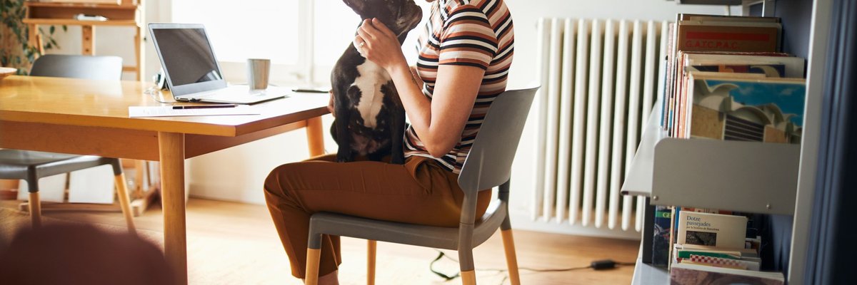 A woman sitting in her home office snuggling with a dog on her lap.