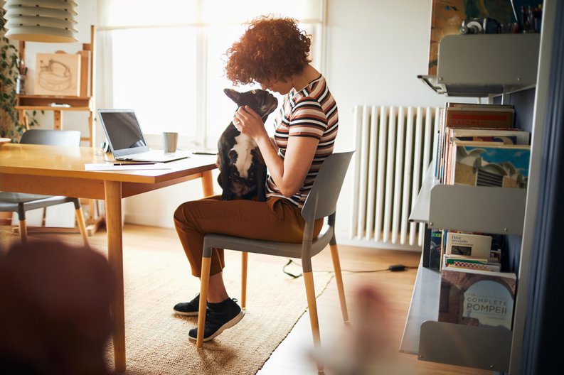 A woman sitting in her home office snuggling with a dog on her lap.