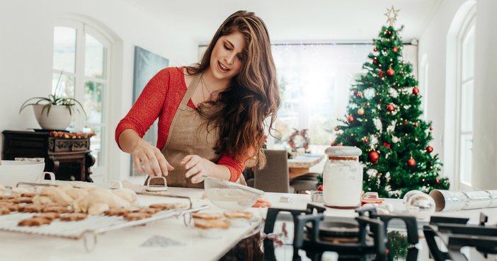 A woman baking cookies in her kitchen with a Christmas tree in the background.