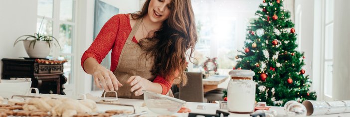 A woman baking cookies in her kitchen with a Christmas tree in the background.