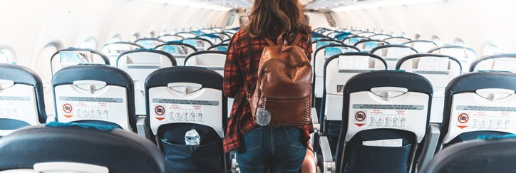 A woman wearing a backpack and walking down the center aisle of an empty airplane.