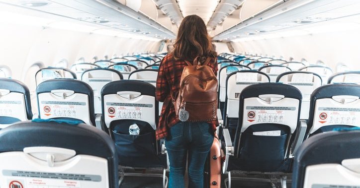 A woman wearing a backpack and walking down the center aisle of an empty airplane.