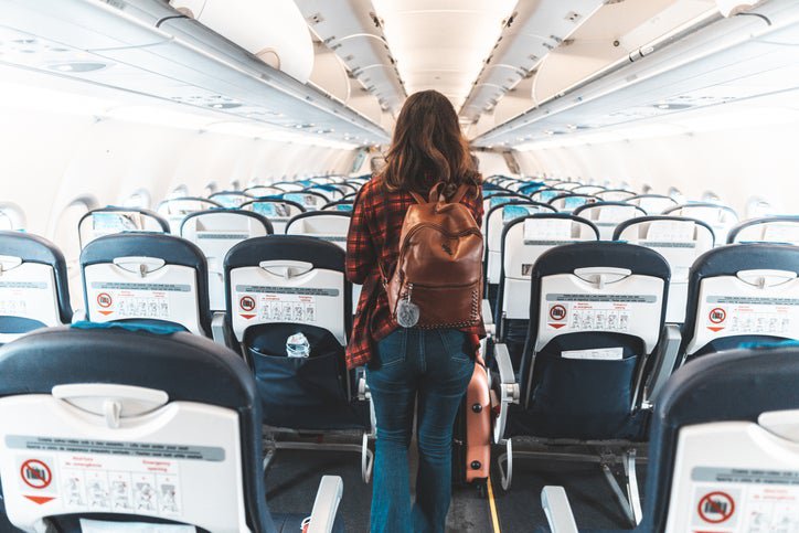 A woman wearing a backpack and walking down the center aisle of an empty airplane.