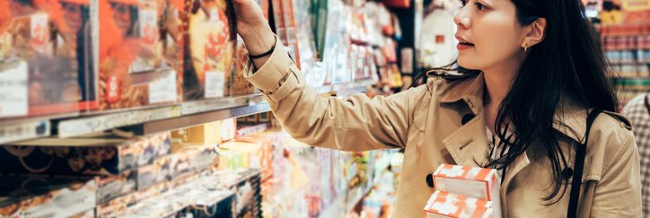A woman browsing the shelves of a store and picking out boxes of holiday sweets.
