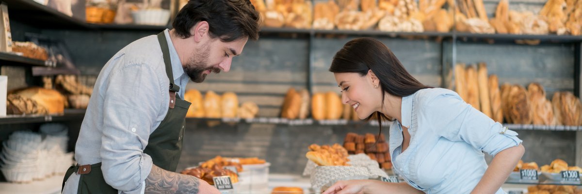 A male cashier helping a woman pick out a pastry at a bakery.