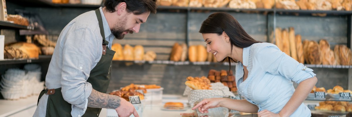 A male cashier helping a woman pick out a pastry at a bakery.