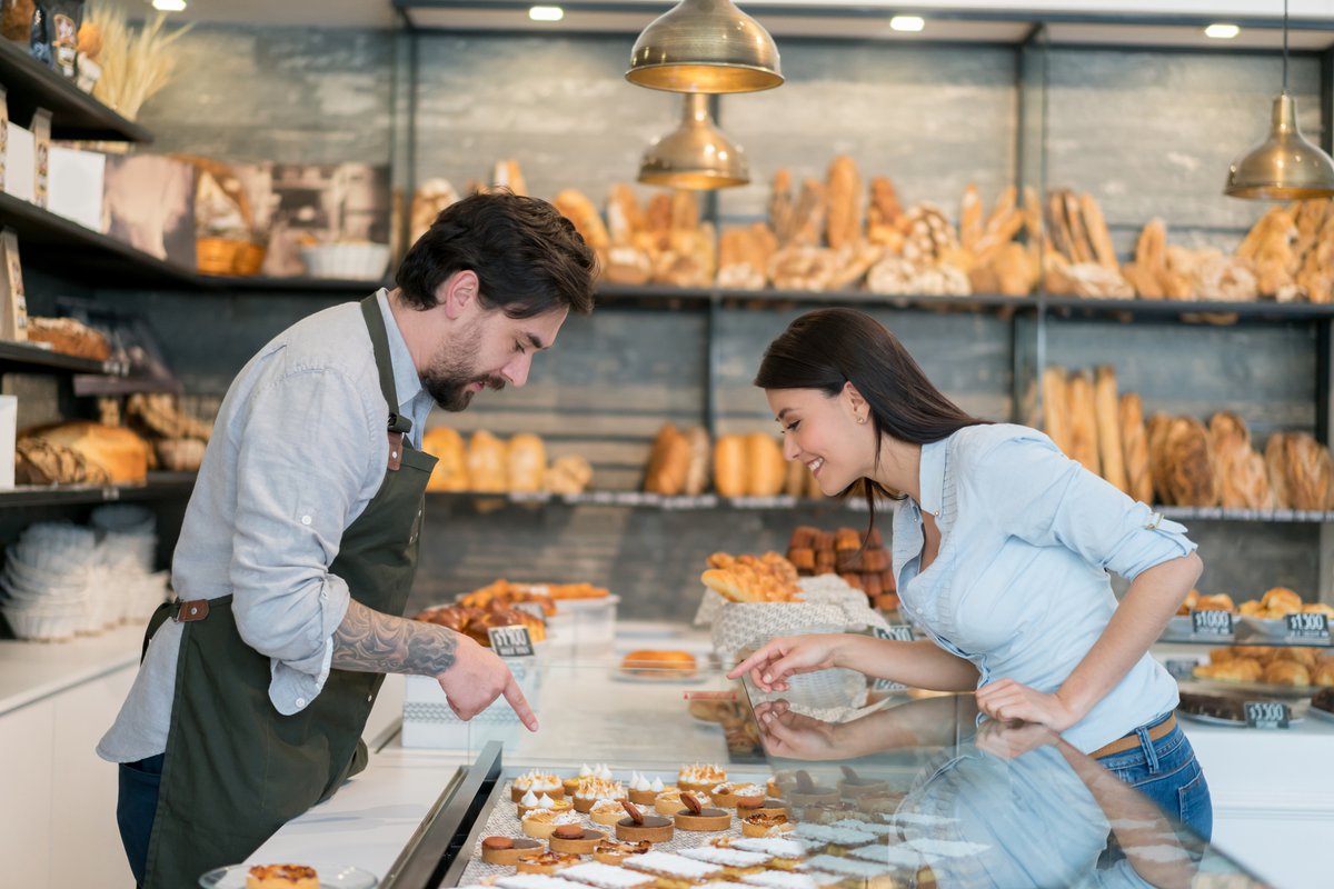 A male cashier helping a woman pick out a pastry at a bakery.