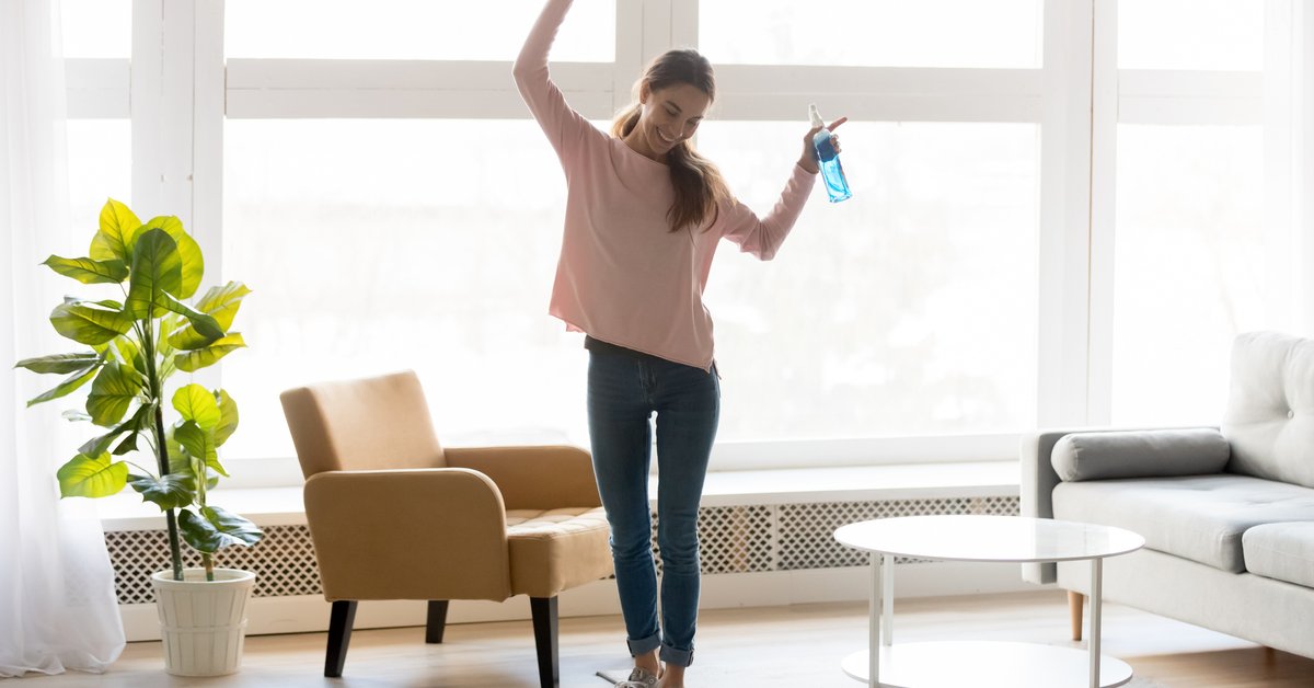 A smiling woman dancing around and cleaning her apartment.