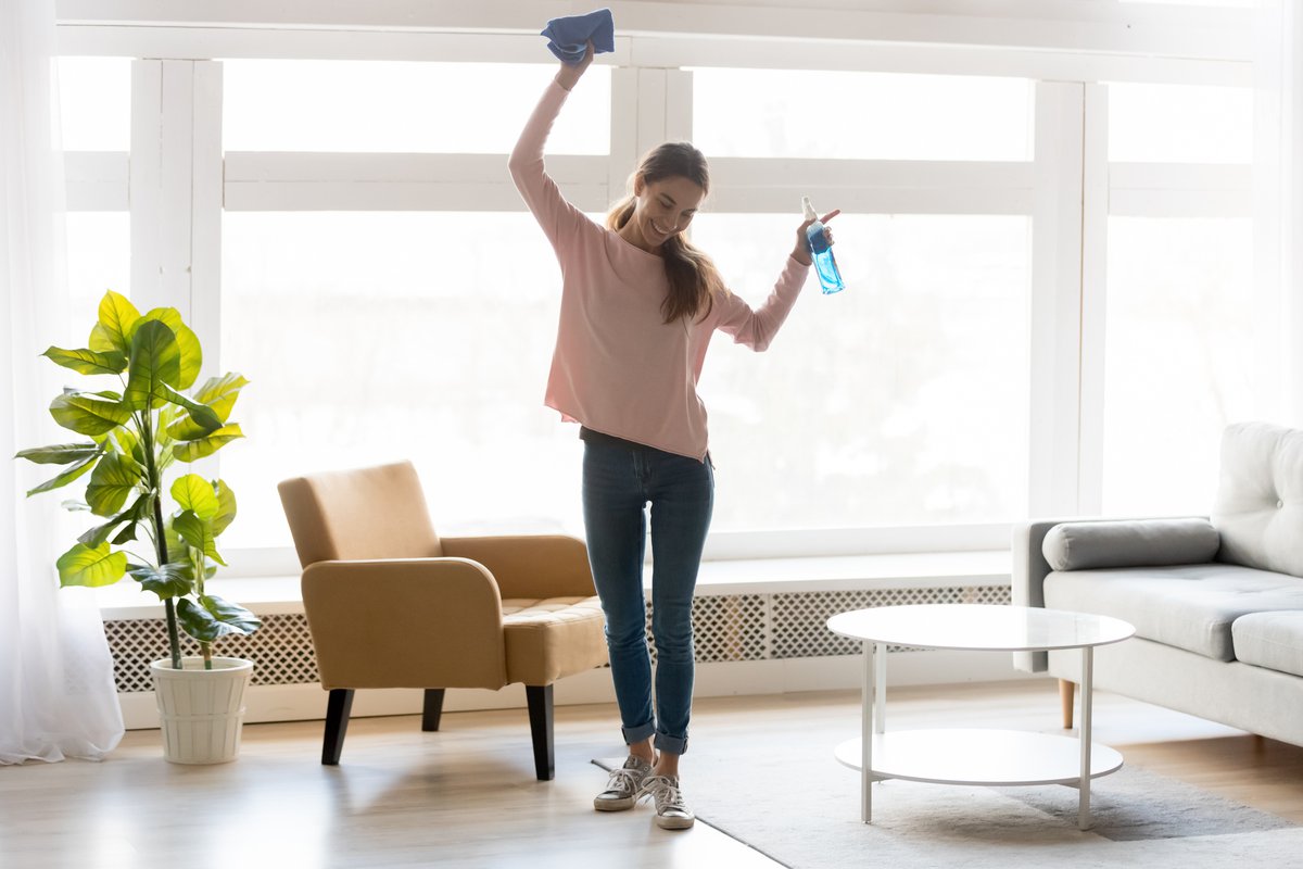 A smiling woman dancing around and cleaning her apartment.