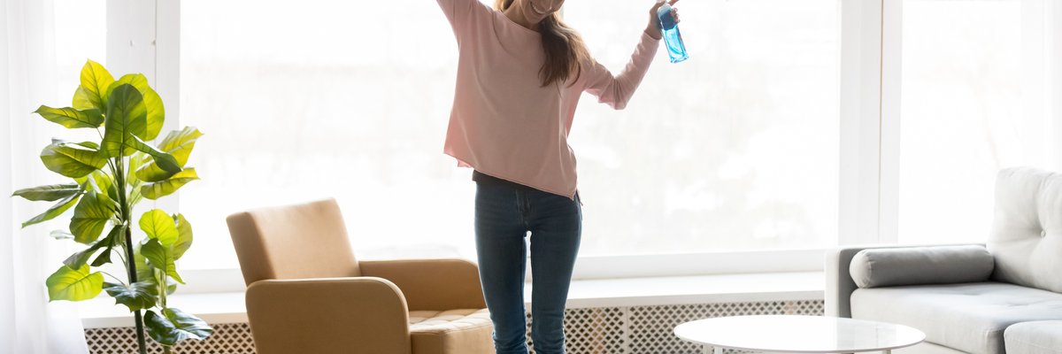 A smiling woman dancing around and cleaning her apartment.