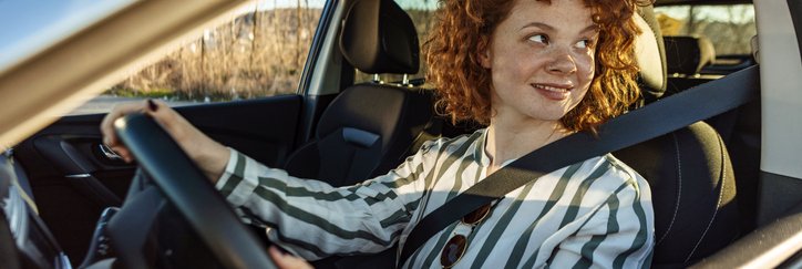 A smiling woman sitting in the driver's seat of a car.