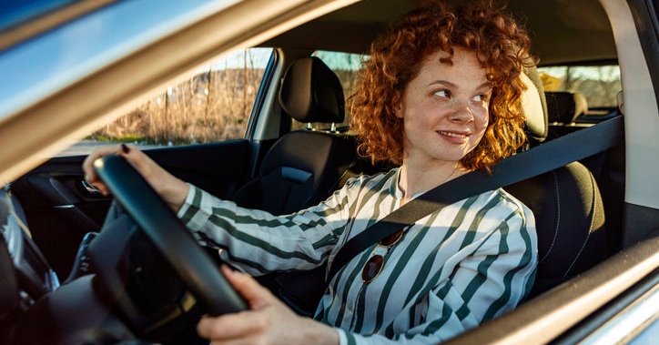 A smiling woman sitting in the driver's seat of a car.