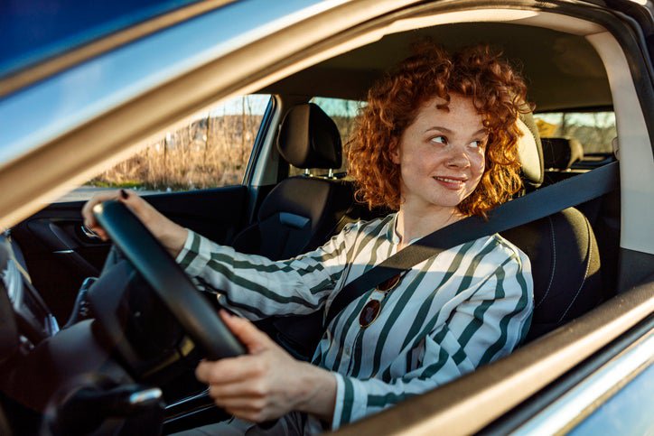 A smiling woman sitting in the driver's seat of a car.