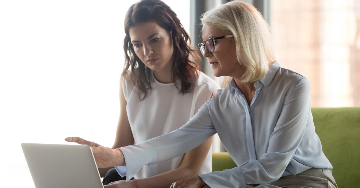A financial advisor and her female client sitting together on a couch and looking at a laptop.