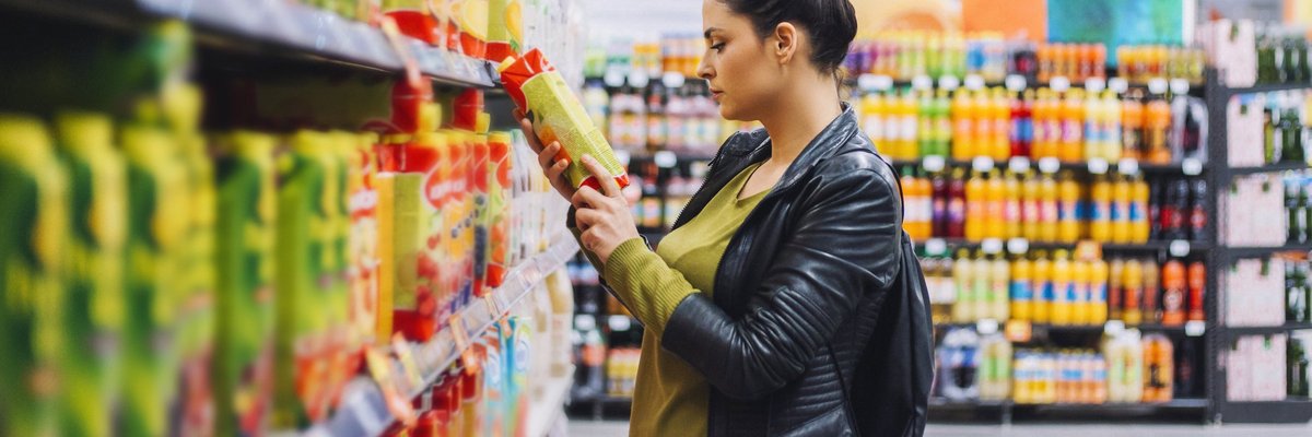 A woman comparing prices on an item while grocery shopping.