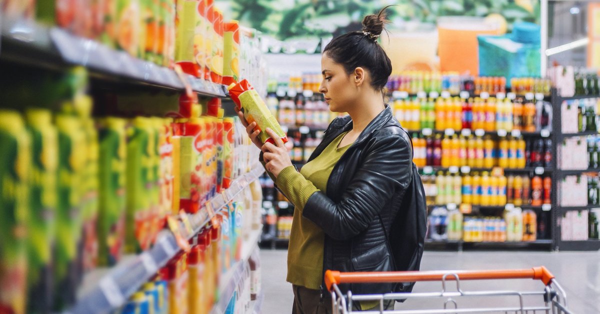 A woman comparing prices on an item while grocery shopping.