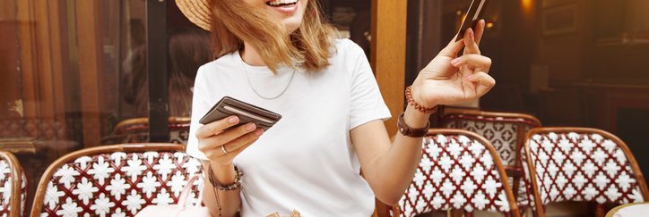 A smiling woman handing her credit card for payment while seated at an outdoor cafe table.