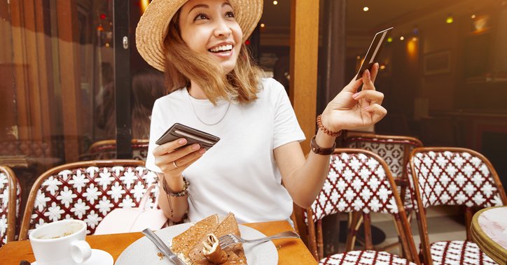 A smiling woman handing her credit card for payment while seated at an outdoor cafe table.