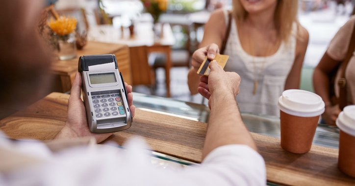 A smiling woman handing her credit card to a coffee shop cashier.