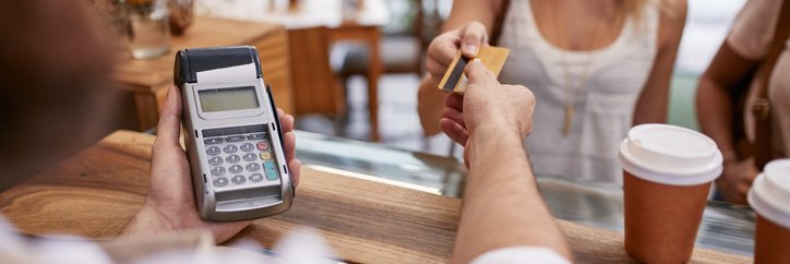 A smiling woman handing her credit card to a coffee shop cashier.