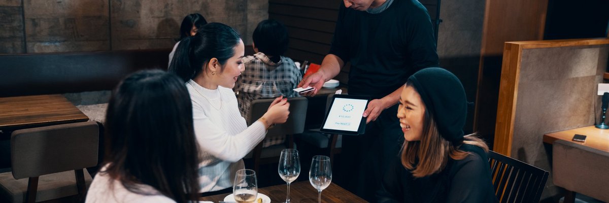 Three women dining at a restaurant while one hands her credit card to the waiter.