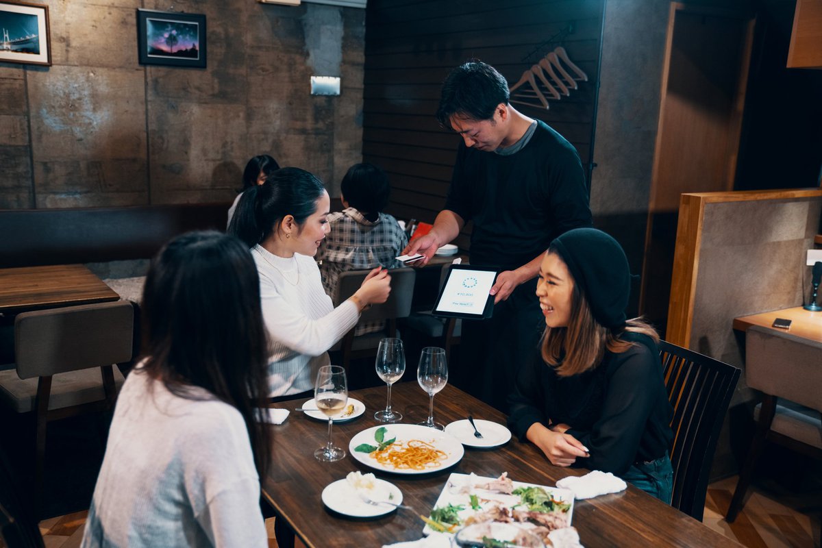 Three women dining at a restaurant while one hands her credit card to the waiter.