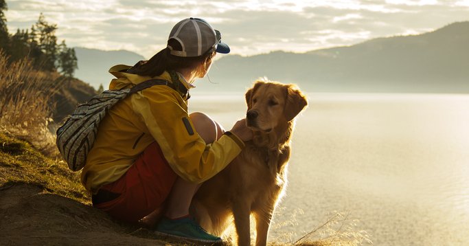 A woman hiking around a lake with her dog and taking in the view over the water at sunset.