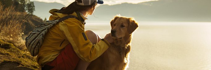 A woman hiking around a lake with her dog and taking in the view over the water at sunset.