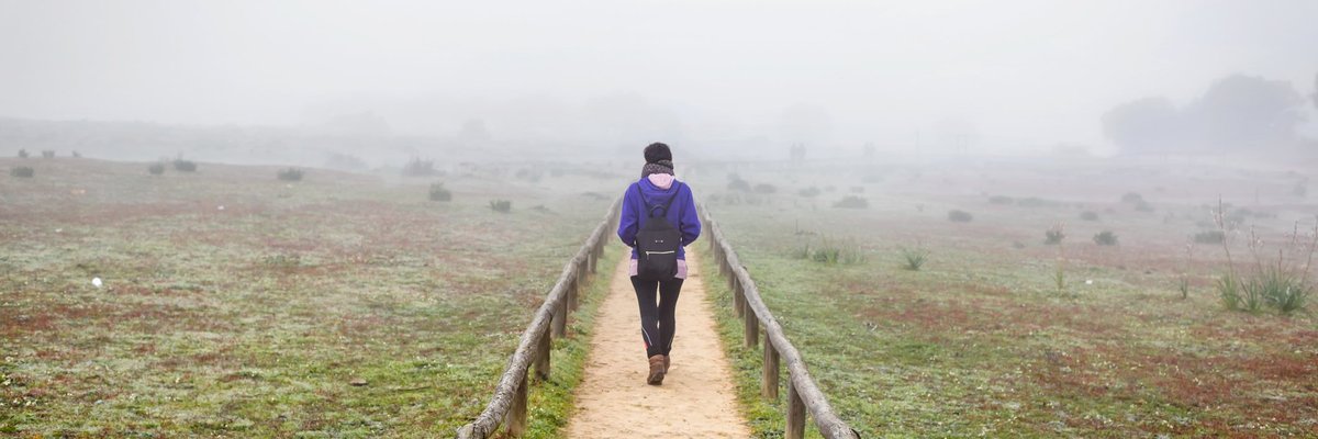 A woman hiking down a dirt path through a foggy field