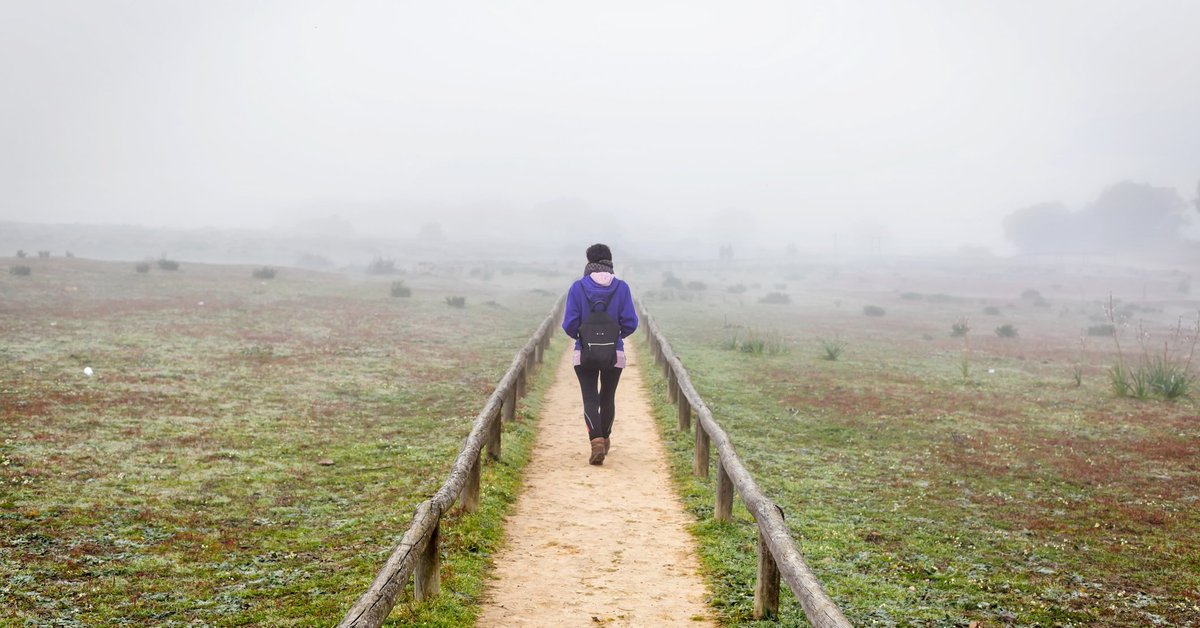 A woman hiking down a dirt path through a foggy field