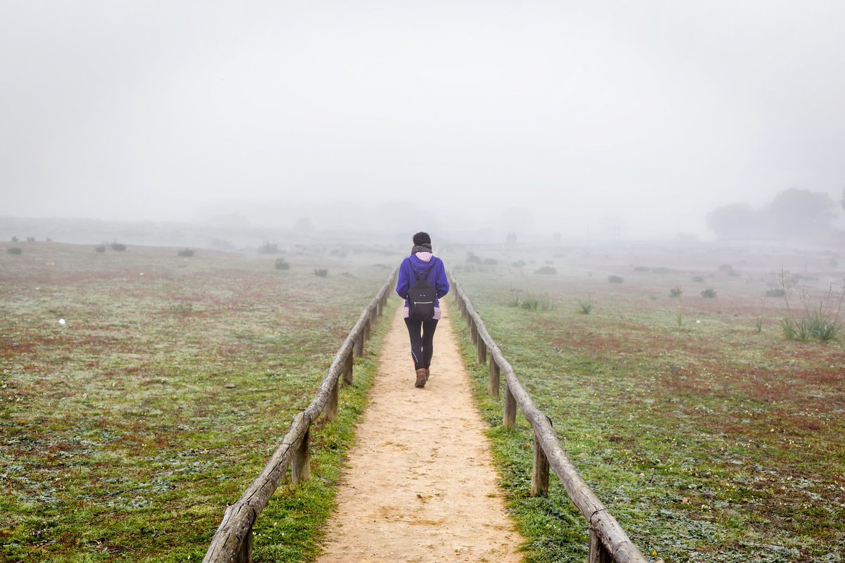 A woman hiking down a dirt path through a foggy field