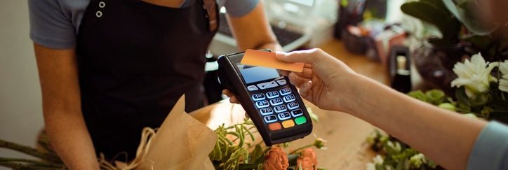 A woman tapping her credit card on a payment reader being held out by a florist in a flower shop.