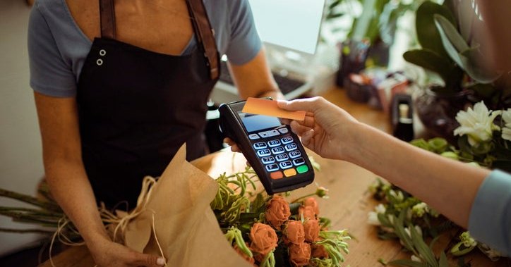 A woman tapping her credit card on a payment reader being held out by a florist in a flower shop.