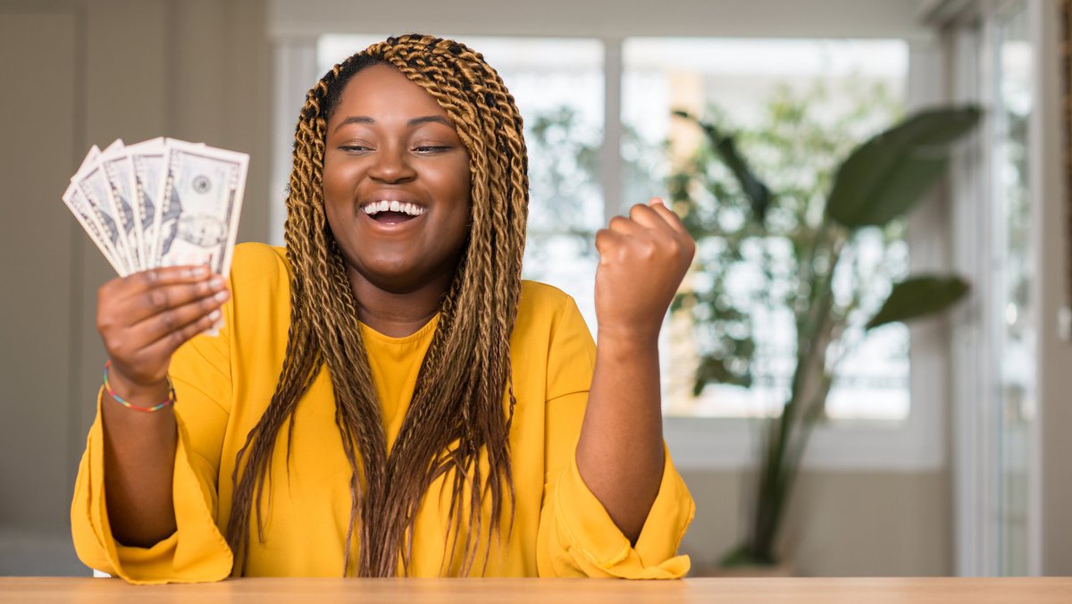 A woman holding a handful of money and pumping her fist in happiness.