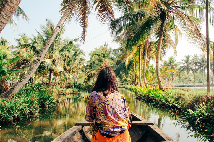 A woman sitting in the front of a row boat on a river surrounded by palm trees.
