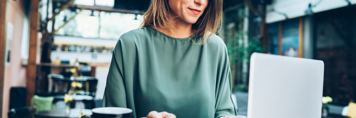 A woman in a cafe sitting at a table with her laptop and holding a credit card.