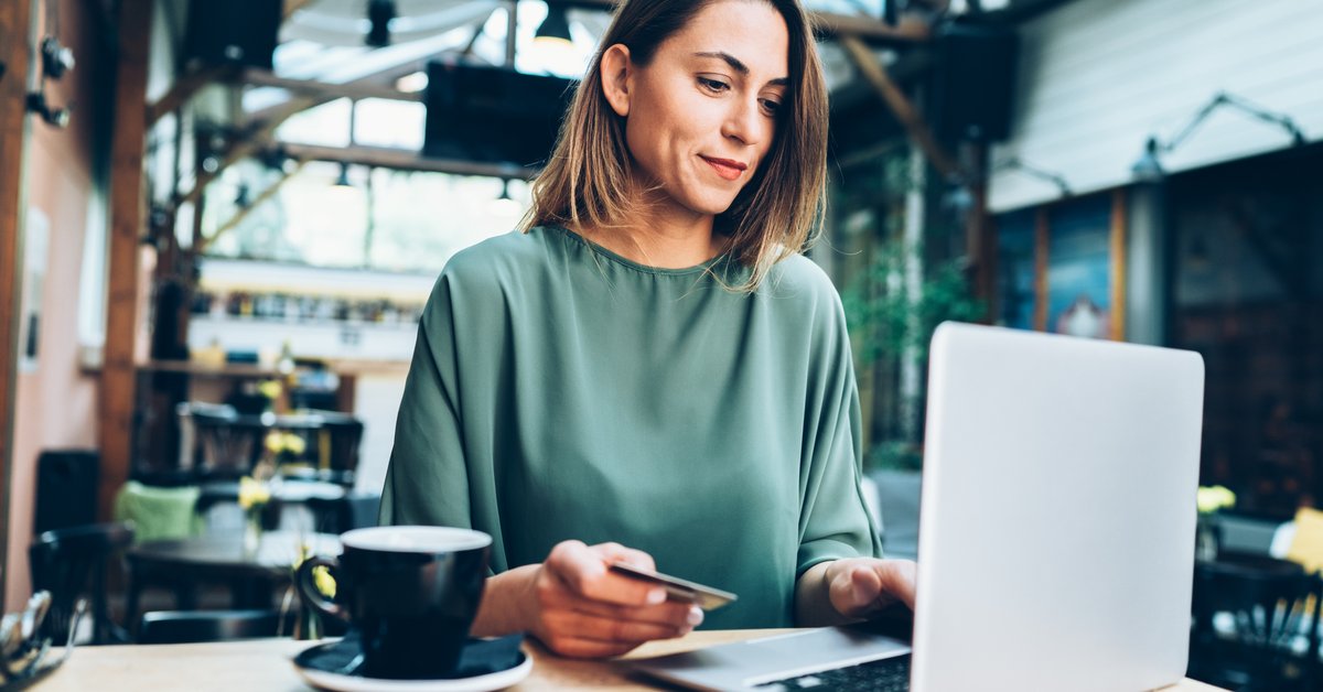 A woman in a cafe sitting at a table with her laptop and holding a credit card.