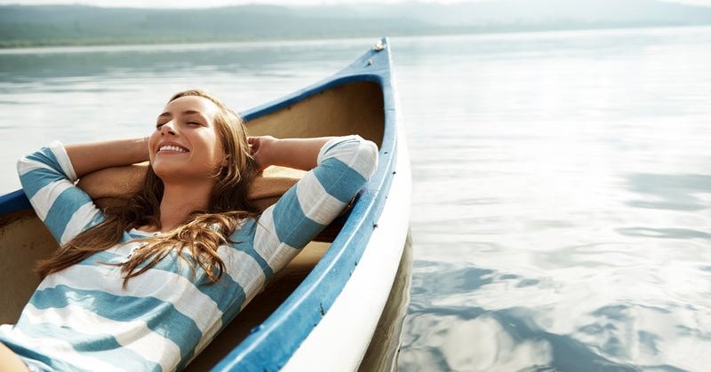 A smiling woman laying back in a canoe on a lake on a sunny day.