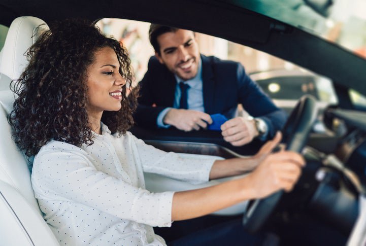 A woman sitting in the driver's seat of a new car and talking to a salesman through the window.