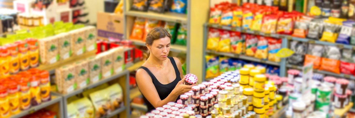 A woman looking at jars of food in an empty grocery store.