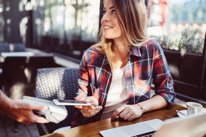 A woman sitting in a restaurant and tapping her smart phone on a payment reader.