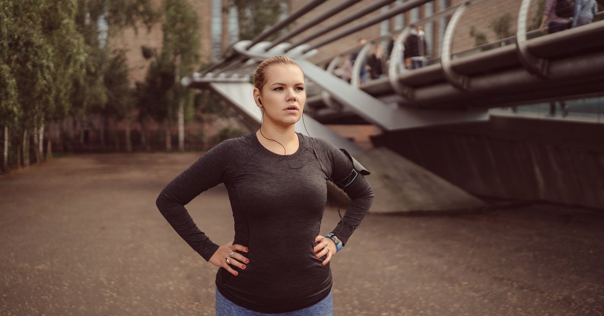 A woman in running gear standing outside with her hands on her hips.