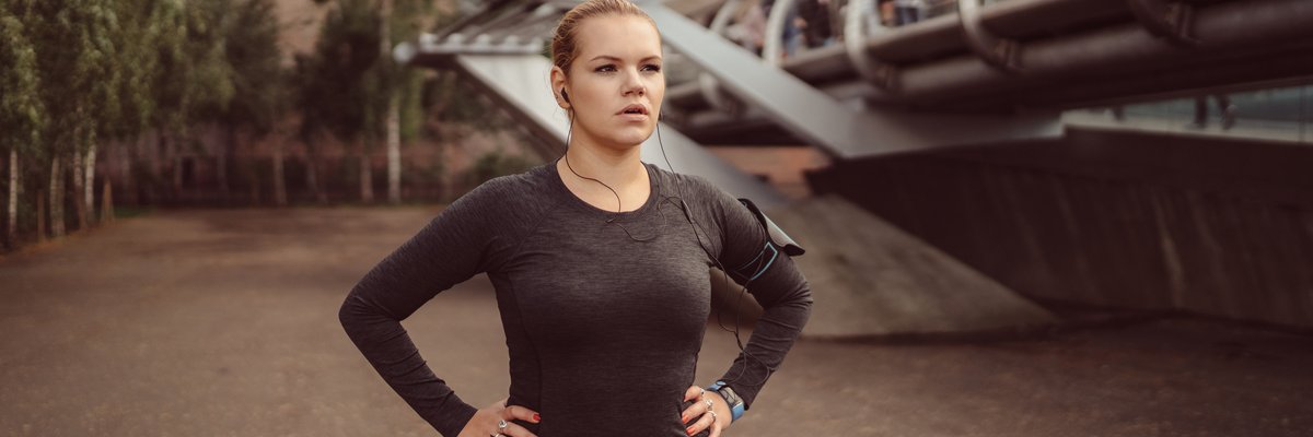 A woman in running gear standing outside with her hands on her hips.