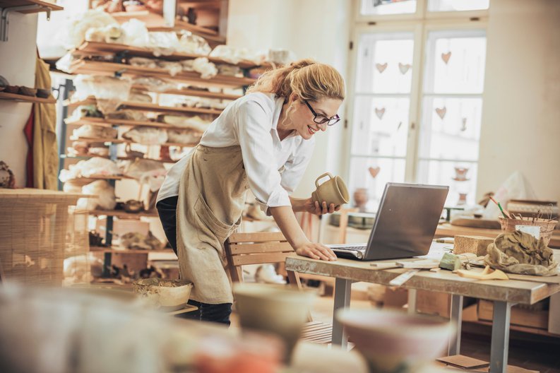 A woman looking at her laptop in her pottery studio.